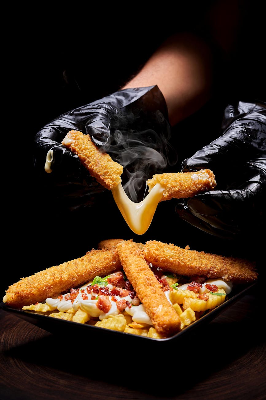 hands in gloves holding nuggets with cheese over plate
